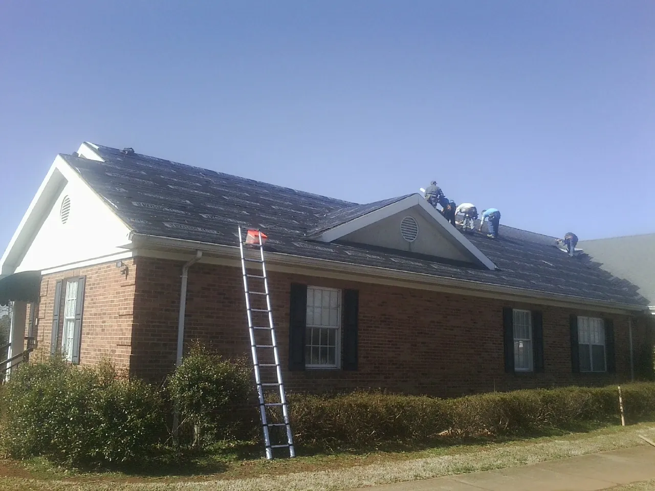 Crew tearing shingles off a brick ranch roof with a ladder set — Metal Roof Repair work by our crew in Micro