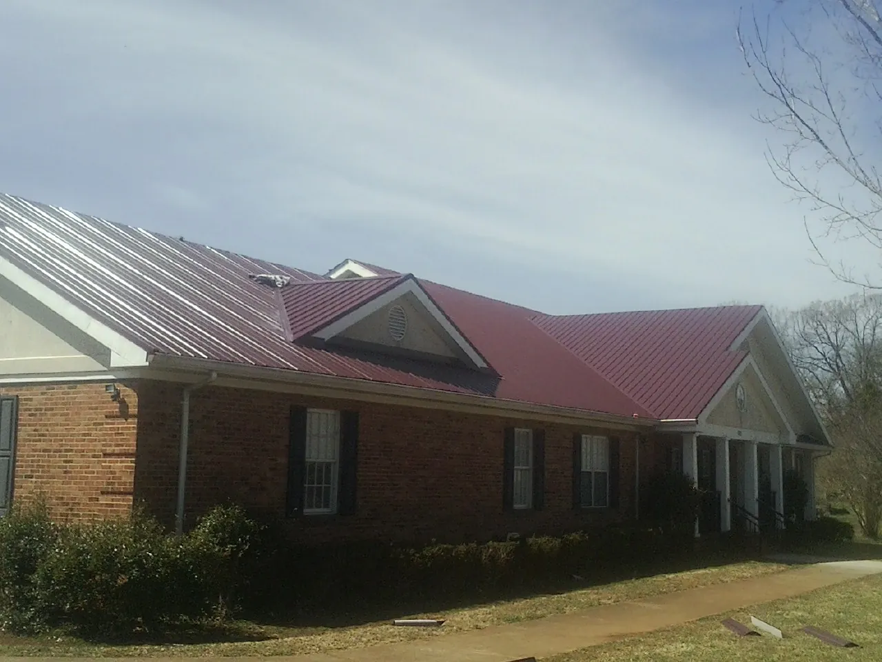 Red metal roof with gabled entries on a long brick building, from a Hail Damage Roof Repair job in Micro