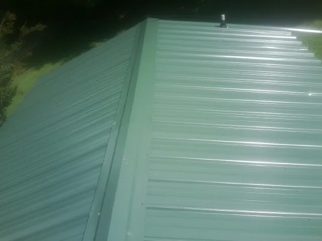 New green metal panels meeting at the ridge of a roof — Flat Roof Repair work by our crew in Micro