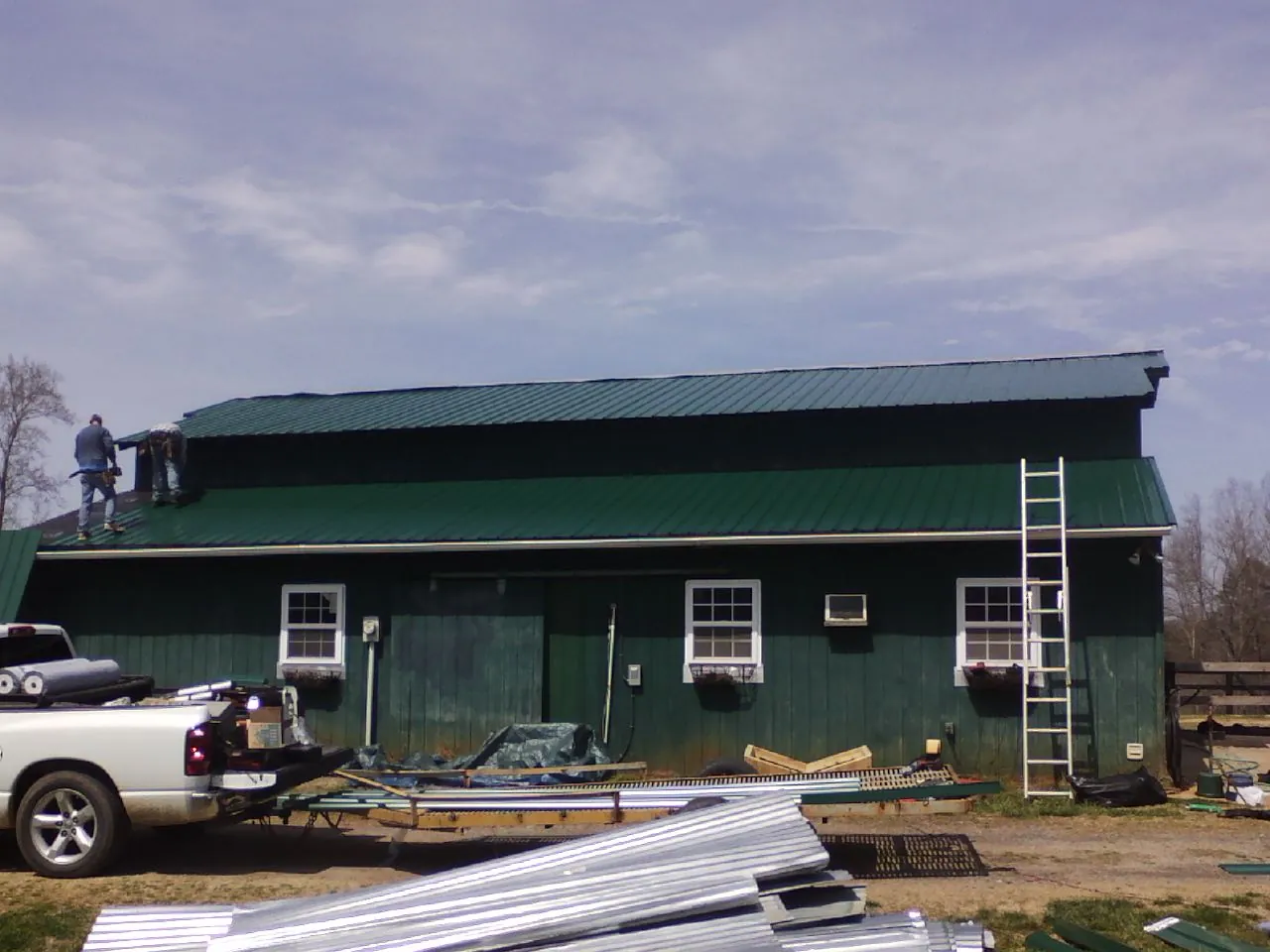 Crew installing green metal roofing on a large green barn in Micro